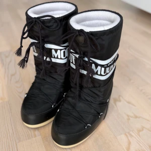 Svarta Moon Boots 35/38 köp eller byt - Säljer ett par klassiska svarta Moon Boots med vit logga och snörning framtill. Dom är knappt använda och dom är som i nytt skick🩷går att köpa eller byta men kontakta vid byte🩷