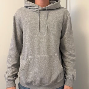 Grå hoodie från H&M, relaxed fit - Säljer en enkel och stilren grå hoodie från H&M i relaxed fit. Tröjan har huva med snörning, magficka och långa ärmar. Perfekt för chill dagar eller när du vill ha något bekvämt och snyggt på dig.
