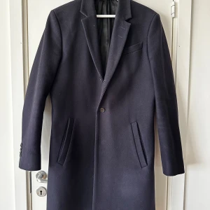Tiger of Sweden - Mens wool coat  - Herr rock från Tiger of Sweden i dark navy.  Size: 48  70 % återvunnen ull 27 % polyester 3 % andra fibrer Slim Fit Rock i italiensktillverkad ullmix Tre knappar Slutar mitt på låret Spetsiga slag Snedställda passpoalfickor Överlappande manschettknappar En slits baktill Helfodrad  Använd men i väldigt bra skick.  Nypris: 5999 sek Mitt pris: 1999 sek  https://www.tigerofsweden.com/se/sv/herr/tidigare-kollektioner/cempsey-rock-104848284.html