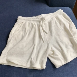 Vita frottéshorts med snörning - Mysiga vita shorts i mjuk frotté med elastisk midja och snörning framtill. De har två sidofickor och en bakficka, perfekt för chill dagar eller strandhäng. Lätta och sköna att bära under varma sommardagar. Knappt använda☺️