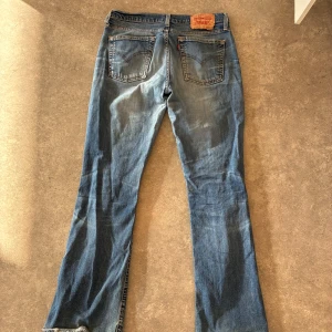 Levi's blå bootcut jeans - Snygga blå jeans från Levi's med klassisk bootcut-passform. Jeansen har fem fickor, slitningar och en cool tvättad look. Tillverkade i robust denim med detaljer som kopparfärgade nitar och Levi's patch bak. Perfekta för dig som gillar retrostil och bekväma jeans.