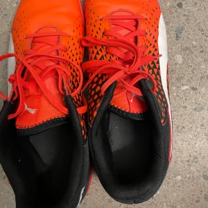 Röda PUMA EvoSpeed fotbollsskor - Snygga PUMA EvoSpeed fotbollsskor i rött med svarta och vita detaljer. Skorna har coolt grafiskt mönster, snörning och platt sula. Perfekta för dig som vill sticka ut på planen. Tillverkade i syntetmaterial för lätt känsla och bra grepp.