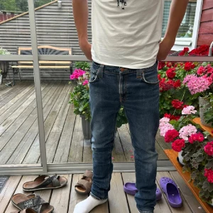 Blå jeans från Nudie Jeans, slim fit - Säljer ett par klassiska blå jeans från Nudie Jeans med snygga slitningar och kontrastsömmar. Modellen är slim fit med normal midja och raka ben. Jeansen har fem fickor och detaljerade bakfickor med Nudie-loggan. Perfekta för en avslappnad och stilren look. Storleken på byxorna är w34 l32 men skulle snarare säga w30 l32 för modellen har den storleken och dom passar utmärkt🤩