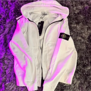 Vit hoodie från Stone Island - Säljer en clean vit hoodie från Stone Island med dragkedja och klassisk patch på vänster ärm. Tröjan har huva, fickor framtill och ribbade muddar. Passar M men även S. Vid snabb affär kan priset diskuteras. Tveka inte att skriva om du har frågor 