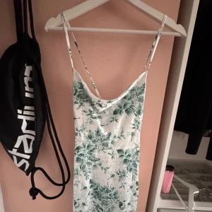 Vit och grön blommig medellängd klänning - Supersöt medellängd med tunna axelband och v-ringad hals. Klänningen är vit med grönt blommigt mönster och har även detaljer med trollsländor. Materialet känns lätt och svalt, perfekt för varma dagar. Sitter snyggt och har en feminin siluett.