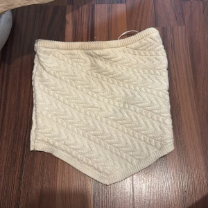 Stickad beige top från Bershka XS - Supersöt stickad top från Bershka i beige med kabelstickat mönster. Topen är kort och har en unik spetsig nederkant framtill. Perfekt för dig som gillar mysiga och trendiga plagg med lite extra detalj. Använd 3gngr