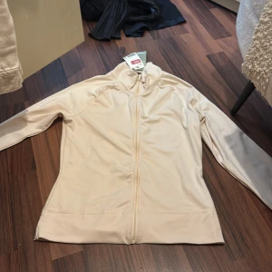 Beige ziptröja i polyester, strl S - Säljer en stilren beige ziptröja från H&M i storlek S. Tröjan har hel dragkedja framtill, hög krage och långa ärmar. Materialet är mjuk polyester som känns skönt mot huden. Perfekt för lager-på-lager och chill dagar.