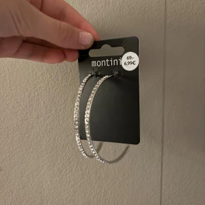 Glittriga silver hoops från Montini - Stora, runda örhängen i silver från Montini med glittriga stenar längs hela bågen. Perfekta för att ge din look extra bling och att sticka ut med. Snyggt och trendigt val för dig som gillar statement-smycken.
