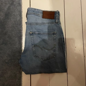 Ljusblå tapered jeans från Jack & Jones 29/32 - Säljer ett par ljusblå jeans från Acne Studios i modellen Tapered/Mike. Jeansen har klassisk femficksdesign, raka ben med avsmalnande passform och snygga detaljer som läderpatch bak. Perfekta för dig som gillar stilrena och bekväma jeans.