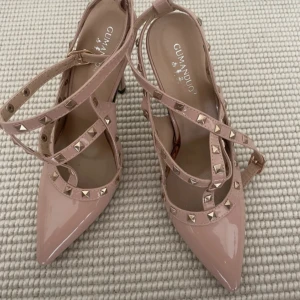 Rosa pumps med nitar och spetsig tå - Snygga ljusrosa pumps med lackad finish och spetsig tå. Skorna har remmar med coola guldfärgade nitar och en smal klack. Perfekta för dig som vill sticka ut med en edgy men feminin stil.