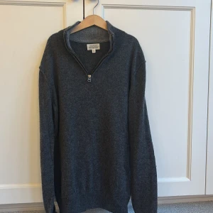 Mörkgrå halvzip-tröja från Hartford -  mörkgrå tröja från Hartford med halv dragkedja vid kragen. Tröjan är långärmad och har ett litet hål i ryggen/ inget man ser 