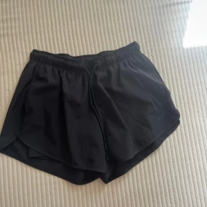 Svarta träningsshorts från Lager 157 - Svarta  shorts från Lager 157 med elastisk midja och snörning. Lätta och luftiga med sportig passform, perfekta för träning eller löpning. Tillverkade i syntetmaterial som andas och torkar snabbt. Stilren design utan mönster eller extra detaljer.