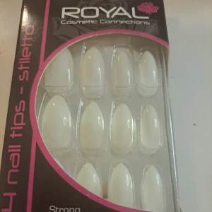 Royal stiletto lösnaglar 24-pack - Säljer ett paket med 24 vita stiletto-formade lösnaglar från Royal Cosmetic Connections. Naglarna är långa och spetsiga, perfekta för en edgy look. Paketet innehåller även 3g nagellim för enkel applicering.