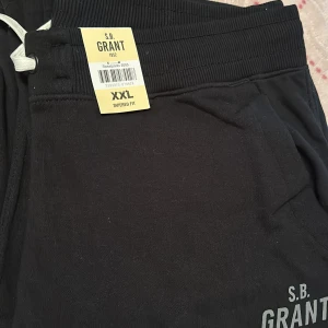 Svarta mjukisbyxor från S.B. Grant - Svarta mjukisbyxor från S.B. Grant med dragsko i midjan och tapered fit. Byxorna har resår i midjan och sidofickor, perfekt för en avslappnad stil.