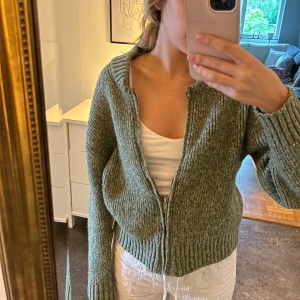 Grön stickad kofta med dragkedja - Mysig grön stickad kofta med dragkedja framtill. Tröjan har långa ärmar och ribbade muddar vid ärmslut och nederkant!!💕