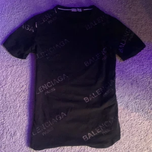 Svart t-shirt från Balenciagạ med logotypmönster - Säljer en svart t-shirt från Balenciạ med tryckt logotypmönster över hela tröjan. T-shirten har rund hals och korta ärmar. Perfekt för dig som gillar exklusiva streetwear-plagg.