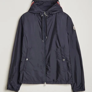 Mörkblå vindjacka med huva från Moncler - Snygg mörkblå vindjacka från Moncler med huva och dragsko. Jackan har dragkedja framtill, två fickor med knappar och Moncler-logga på ärmen. Perfekt för blåsiga dagar. Självklart äkta kan tänka mig gå ner i pris vid snabbt affär. Använd 2-3 gånger. 
