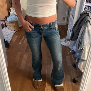 Blå bootcut jeans med låg midja - Säljer ett par klassiska blå jeans med bootcut och låg midja. Jeansen har fem fickor, snygga sömmar och stängs med dragkedja och knapp. Perfekta för dig som gillar en retro vibe och vill ha ett par jeans som sitter snyggt över höften. Storleken är 158/164 och har väldigt stretchigt material. Själv är jag 162
