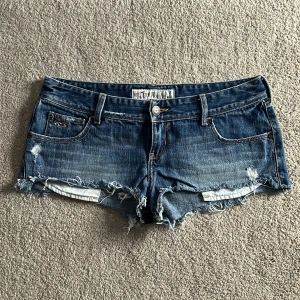 Blå jeansshorts från Hollister - Säljer ett par blå jeansshorts från Hollister med slitna detaljer och fransar längs bensluten. Jättefin modell med låg midja. Perfekta för varma sommardagar!!!