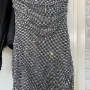 Glittrig silver kortklänning S - Supersnygg glittrig kortklänning i silver med draperad framsida och figurnära passform. Klänningen är axelbandslös och täckt av små paljetter som fångar ljuset. Perfekt för dig som vill sticka ut och glänsa på nästa fest. Aldrig använd, köpt den nyligen😊