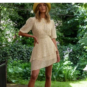 Adoore klänning - Supersöt kortklänning i ljusbeige med små gula blommor, puffiga kortärmar och volangdetaljer. Klänningen är använd få gånger och är i bra skick 