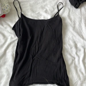 Svart linnetopp från Primark - Enkel och stilren svart linnetopp från Primark med tunna axelband och stretchigt material. Perfekt att matcha med jeans eller kjol för en clean look. Sitter tajt och har en klassisk rak skärning.