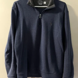 Mörkblå tröja med dragkedja från Polo Ralph Lauren - Säljer en mörkblå långärmad tröja från Polo Ralph Lauren med halv dragkedja och broderad logga på bröstet. Tröjan har en klassisk passform och är tillverkad i mjukt bomullsmaterial. Perfekt för lager-på-lager och stilren vardagslook.