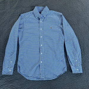 Ralph Lauren skjorta(rutig) - Blå och vitrutig skjorta från Ralph Lauren. Skön och luftig i 100 % bomull. Passar både vardag och fest. Sitter bra utan att vara tajt. Stilren logga på bröstet. Enkelt, snyggt och bekvämt.