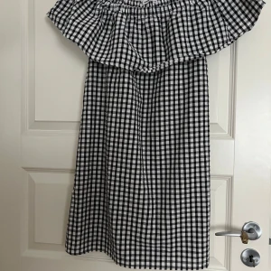 Rutig offshoulder klänning Sinsay XS - Supersöt svartvit rutig offshoulder klänning från Sinsay i storlek XS. Klänningen har volang upptill och är ärmlös, perfekt för varma dagar. Den är kort och har en luftig passform som känns både trendig och bekväm.