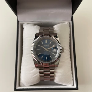 Seiko Oyster Perpetual Datejust herrklocka - Snygg Seiko Oyster Perpetual Datejust med blå urtavla, silverfärgad boett och länkarmband i metall. Klockan har datumvisning och räfflad bezel. Automatisk rörelse synlig genom baksidan. Perfekt accessoar för dig som gillar klassisk stil.