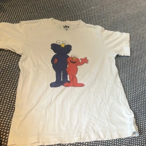 Vit UNIQLO x KAWS Sesame Street t-shirt - Vit t-shirt från UNIQLOs samarbete med KAWS och Sesame Street. Framsidan har tryck med Elmo och KAWS-version av Grover, samt en annan med hela Sesame Street-gänget. Mjukt bomullsmaterial och klassisk passform. Perfekt för dig som gillar streetwear och popkultur.en xs en 9-10 år en 10-11 år. En small och en till xs varje tröja 350 st förutom KAWS peace den kostar endast 150