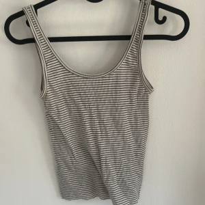 Randig linnetopp från H&M - Säljer en randig linnetopp från H&M Basic i vitt och svart. Toppen har smala axelband och är tillverkad i mjuk bomull, perfekt för varma dagar eller som lager under andra plagg.