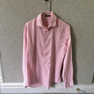 J.Lindeberg skjorta - Säljer en klassisk långärmad skjorta från j.lindeberg i färgen rosa och vitt med tunna ränder. Skjortan har knappar framtill och en mjuk krage. Perfekt för dig som gillar stilrena och tidlösa plagg. Parfekt till sommaren🔥