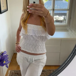 Vit top - Säljer en söt vit topp med broderade detaljer och volanger. Toppen har halterneck med gula band och smockad midja för en bekväm passform. Perfekt för varma dagar och ger en romantisk känsla. Has holes for arms and can be worn as a off shoulder top!