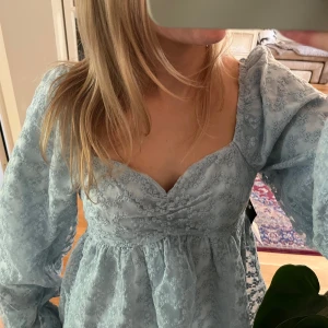 Ljusblå broderieklänning - Supersöt ljusblå klänning med v-ringning och långa puffärmar. Klänningen har spetsdetaljer och en lätt utställd kjol. Jag vill egentligen inte sälja men lägger ut fen då jag tyvärr inte fått användning för den.. Helt ny! lapp är kvar❤️❤️