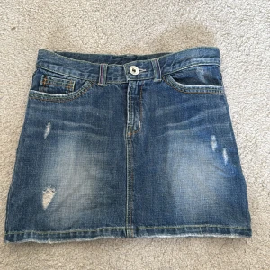 Jeanskjol - Säljer en klassisk blå jeanskjol med slitna detaljer och fickor både fram och bak. 