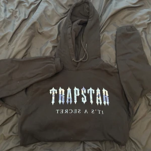Trapstar hoodie - Säljer en svart hoodie från Trapstar med tryck i vitt och blått på bröstet, cond 8.5/10, givetvis äkta köpt från Trapstar, kvitto finns. Strl M men passar S.