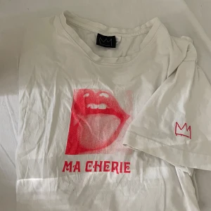 MA Cherire hov1 T-shirt' - Vit t-shirt med röd grafisk print av en öppen mun och texten 'MA CHERIE' framtill. Liten röd krona broderad på ärmen. Rund halsringning och avslappnad passform. Perfekt statement-plagg för en cool look.