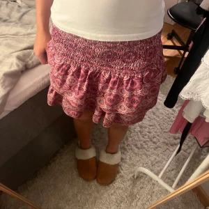 Rosa mönstrad volangkjol - Supersöt kort kjol i rosa med volang och smockad midja. Sitter skönt och perfekt för en sommar dag🥰