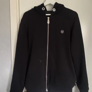 Svart hoodie från Philipp Plein - Svart hoodie från Philipp Plein med ett stort tryck på baksidan och många snygga detaljer! Den är i storlek L men passar M och är självklart i ett äkta exemplar. Är öppen för era frågor och funderingar och priset för denna är ej hugget i sten! 