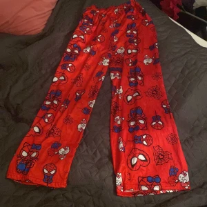 Röda Spiderman x Hello Kitty mjukisbyxor - Säljer ett par röda mjukisbyxor med Spiderman och Hello Kitty-motiv över hela byxorna. Byxorna har resår i midjan och är i ett mjukt, skönt material. Perfekta för chill dagar hemma eller som pyjamasbyxor. Färgglada och unika med coolt tryck!