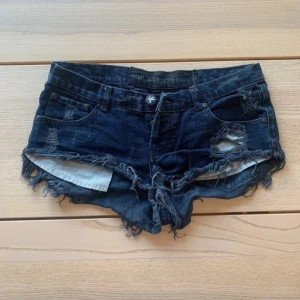 Mörkblå slitna jeansshorts One Teaspoon - Snygga mörkblå jeansshorts från One Teaspoon med råa, fransiga kanter och slitna detaljer både fram och bak. Klassisk femficksmodell med knapp och dragkedja. Perfekta för sommaren och ger en cool, avslappnad vibe. Storlek S-M💕💕