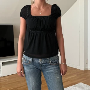 Svart kortärmad blus  - Säljer en svart blus med fyrkantig ringning och korta puffärmar. Blusen har en lös passform och fina rynkade detaljer under bysten. Perfekt att styla med jeans eller kjol.