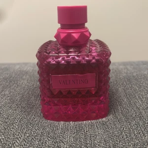 Valentino parfym i rosa flaska - Säljer en lyxig parfym från Valentino i en cool, fyrkantig rosa flaska med nitar och matchande rosa kork. Flaskan har en modern design och känns riktigt exklusiv. Perfekt för dig som gillar snygga detaljer på sminkbordet.