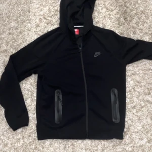 Svart Nike tech fleece kofta (NYA) - Säljer en helt ny oanvänd Nike tech fleece den nya versionen då den är lite för stor på mig. Den passar dig som har storlek M på tröjor! Jag har inga husdjur och röker ej så rökfri lukt och pälsfritt! Modellen är 178 cm lång och 60 kg
