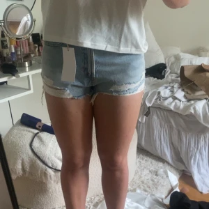 Ljusblå jeansshorts med slitningar - Snygga ljusblå jeansshorts med hög midja och råa, fransiga kanter. Shortsen har slitna detaljer framtill och klassiska bakfickor. Perfekta för sommardagar och ger en avslappnad vibe. stl 40 men passar mig med 38/36💗💗💗