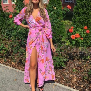 Lång blommig omlottklänning i rosa - Säljer en superfin lång omlottklänning i rosa med blommigt mönster och knyt i midjan. Klänningen har långa ärmar och en snygg slits framtill. Perfekt för sommarens alla tillfällen! En gammal modell från BikBok, men använts 2 gånger.