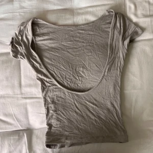 T-shirt med öppen rygg - Säljer en snygg grå topp med korta ärmar och en djup öppen rygg. Perfekt för sommardagar eller en utekväll. Toppen är i ett mjukt och stretchigt material som sitter tight och bekvämt. Passar bra till både jeans och kjol! Tyvärr så har sömmen gått upp på ena armen därav det lägre priset☺️