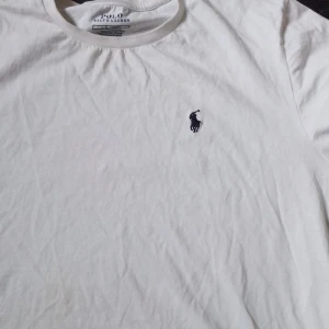 Vit t-shirt från Polo Ralph Lauren. Säljer den billig för att den har fått fläckar på sig. - Klassisk vit t-shirt från Polo Ralph Lauren med rund hals och den ikoniska broderade loggan på bröstet. Perfekt basic-plagg med normal passform och mjukt bomullsmaterial.