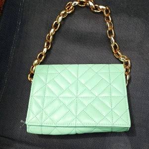 Mintgrön quiltad axelväska med guldkedja - Säljer en mintgrön quiltad axelväska med en chunky guldfärgad kedja som axelrem. Väskan har ett elegant rutmönster och stängs med magnetlås. Perfekt för dig som vill sticka ut med en färgglad accessoar.